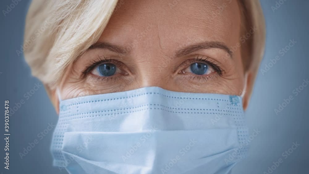close up of middle aged woman with blue eyes in medical mask looking at camera close up of middle aged woman with blue eyes in medical mask looking at camera