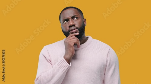 Young African American man thinking and looking up, on yellow background
