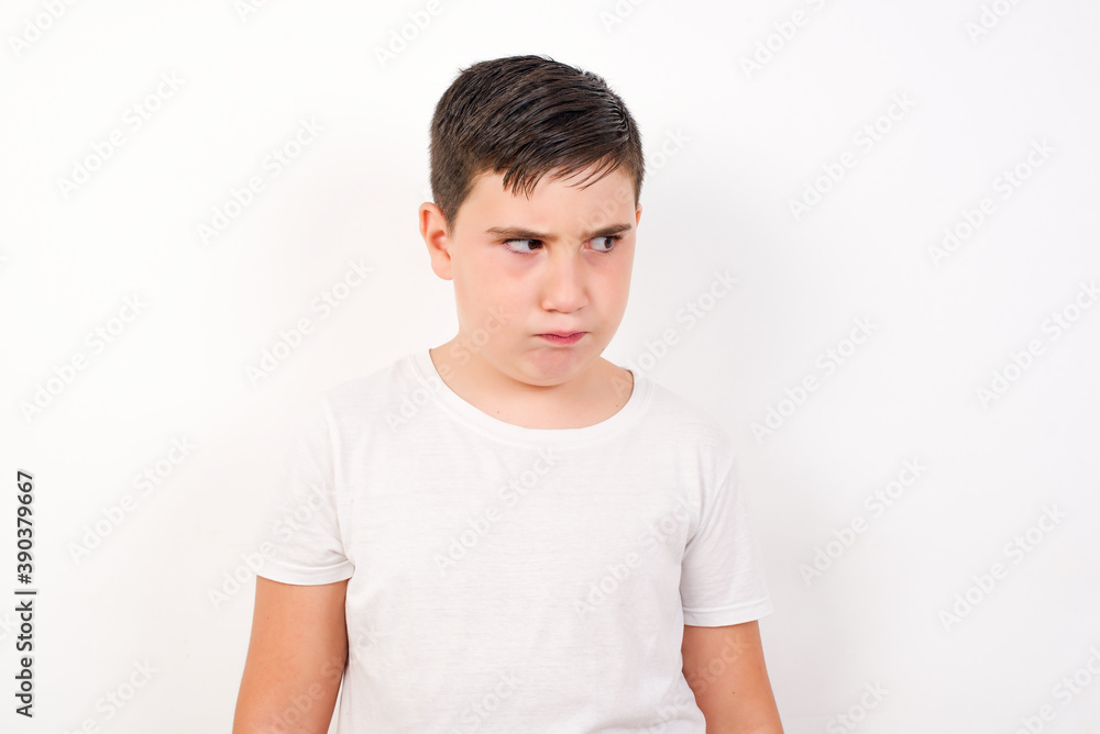 Amazed puzzled Caucasian young boy standing against white background , curves lips and has worried look, sees something awful in front. Amazed puzzled Caucasian young boy standing against white background , curves lips and has worried look, sees something awful in front.