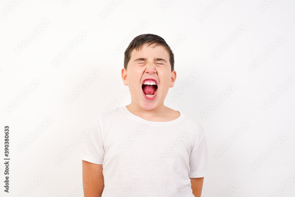 Stressful Caucasian young boy standing against white background screams in panic, closes eyes in terror, keeps hands on head, finds out terrified news, can't believe it. Stressful Caucasian young boy standing against white background screams in panic, closes eyes in terror, keeps hands on head, finds out terrified news, can't believe it.