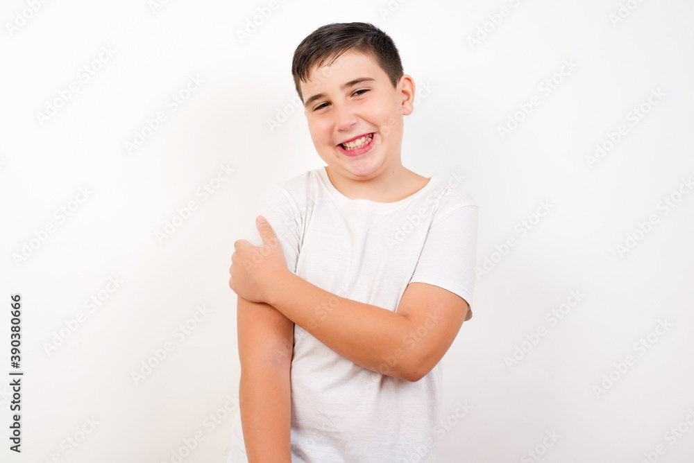 People, lifestyle, youth and happiness concept. Shy pretty Caucasian young boy standing against white background, feeling happy hugging herself. People, lifestyle, youth and happiness concept. Shy pretty Caucasian young boy standing against white background, feeling happy hugging herself.