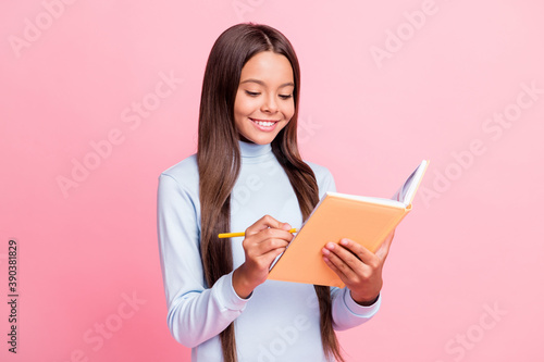 Portrait of lovely focused cheery brown-haired girl writing notes in diary exercise book isolated over pink pastel color background