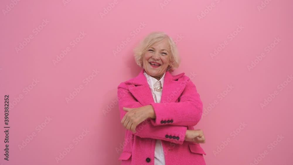 an elderly happy woman in a pink coat gestures with her thumbs up while posing in a Studio against an isolated background. slow-motion video an elderly happy woman in a pink coat gestures with her thumbs up while posing in a Studio against an isolated background. slow-motion video