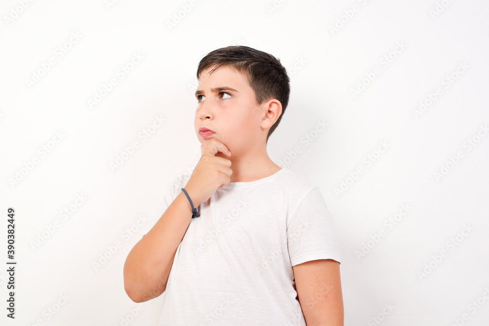 Caucasian young boy standing against white background with thoughtful expression, looks away, keeps hand near face, thinks about something pleasant. Taking decisions concept. Caucasian young boy standing against white background with thoughtful expression, looks away, keeps hand near face, thinks about something pleasant. Taking decisions concept.