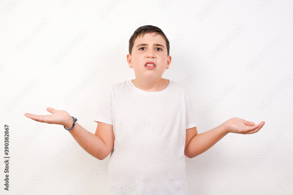 Caucasian young boy standing against white background looks uncertain shrugs shoulders. Caucasian young boy standing against white background looks uncertain shrugs shoulders.