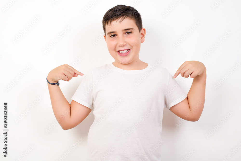 Charming emotive Caucasian young boy standing against white background pointing down or at oneself while smiling joyfully and expressing positive emotions trained a lot wants to show muscles. Charming emotive Caucasian young boy standing against white background pointing down or at oneself while smiling joyfully and expressing positive emotions trained a lot wants to show muscles.