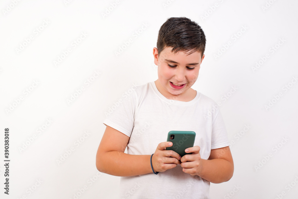 Smiling Caucasian young boy standing against white background using cell phone, messaging, being happy to text with friends, looking at smartphone. Modern technologies and communication. Smiling Caucasian young boy standing against white background using cell phone, messaging, being happy to text with friends, looking at smartphone. Modern technologies and communication.