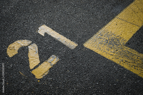 sign on the asphalt, yellow painted number twenty one on grey street, yellow lines like a corner on the road, 
space for text  photo