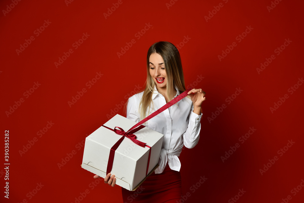 Excited happy screaming blonde woman in white blouse unpacks present big gift box for Christmas and new year 2021 Excited happy screaming blonde woman in white blouse unpacks present big gift box for Christmas and new year 2021