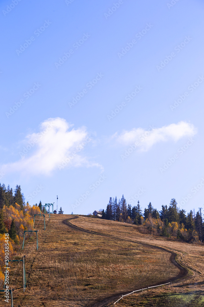 The road leading to the top of the mountain. Natural background of autumn mountains with yellow trees and fir trees with clouds in blue sky