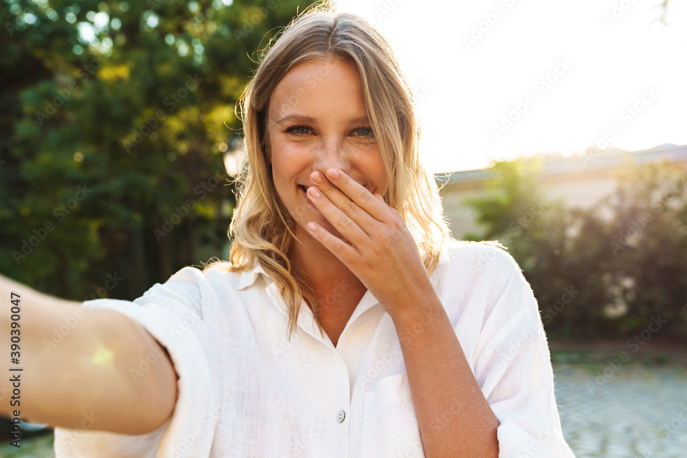Happy woman laughing and taking selfie while walking in green park Happy woman laughing and taking selfie while walking in green park
