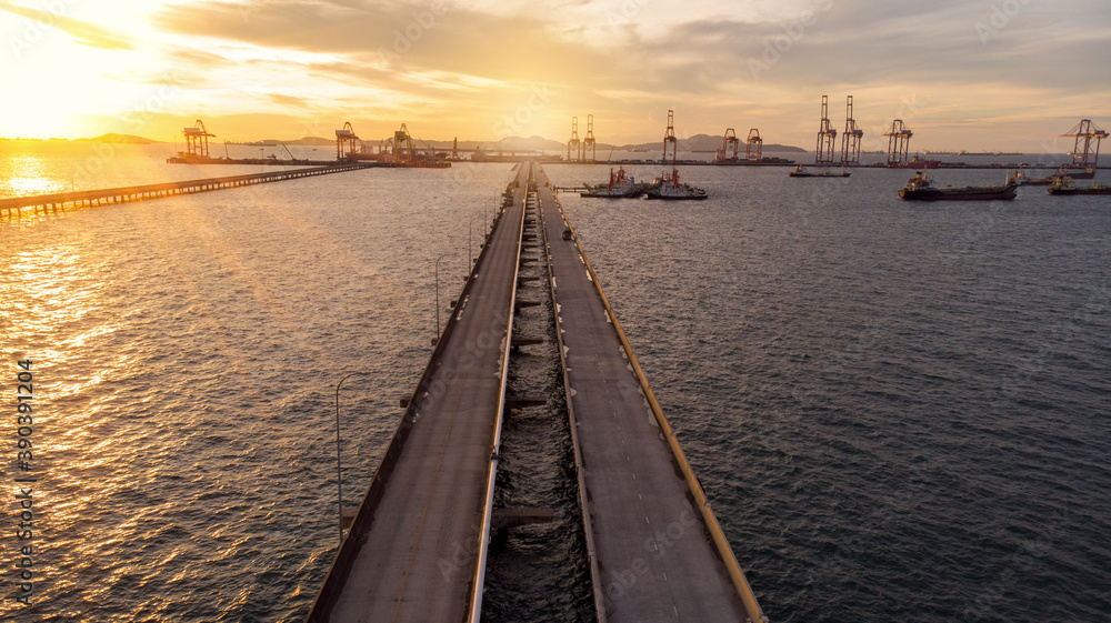 Aerial view of  Bridge for export import cargo to crane at sun set , Bride road to international cargo dock sea port.