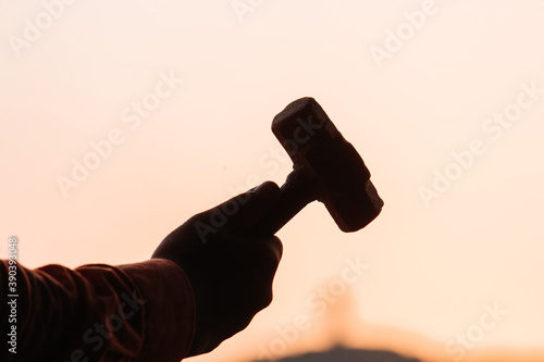 Silhouette of hand holding hammer in front of the sunset