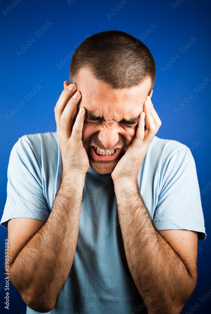Dark short haired man in light blue t shirt, holding hands on his cheeks with closed eyes looking painfull. Studio photo, dark setting. Dark short haired man in light blue t shirt, holding hands on his cheeks with closed eyes looking painfull. Studio photo, dark setting.