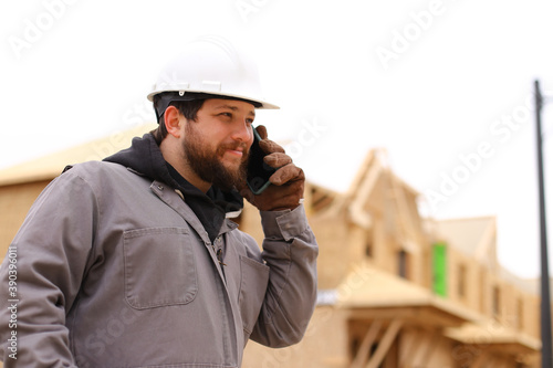Caucasian builder talking by smartphone at construction site.
