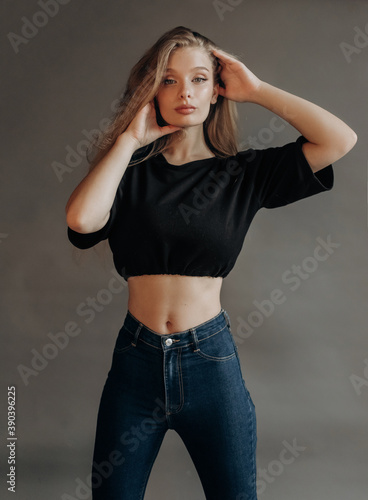 Sexy blonde in a black top and  jeans posing in the studio on a gray background © Yuliia