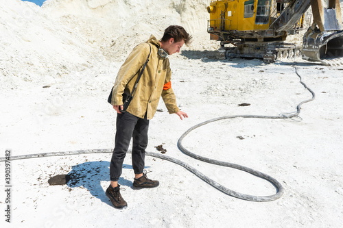 the traveler stands in front of a large excavator. a man stands next to a high-voltage wire in the middle of a white sand industrial quarry.