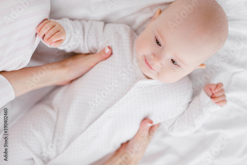 A young Caucasian mother in home clothes holds a newborn baby in a white jumpsuit. Smiles and hugs the child.