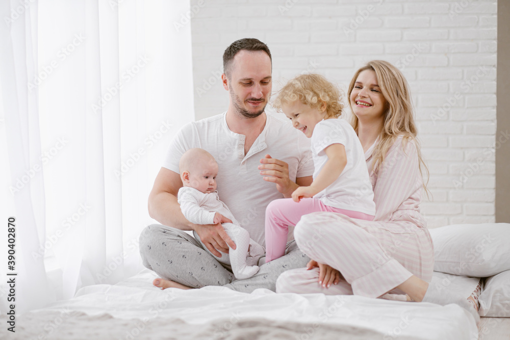 A young Caucasian family with two children daughters in a white home interior. Home clothes. A young Caucasian family with two children daughters in a white home interior. Home clothes.