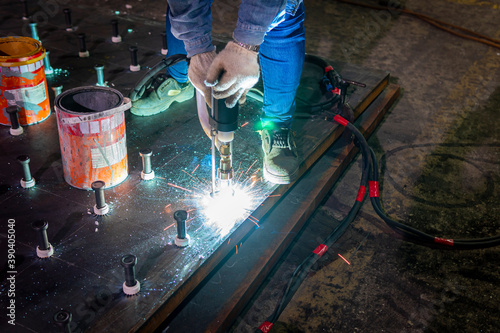 A welder is using a Stud Welding Machine to weld stud bolt on steel plate, at industrial factory.