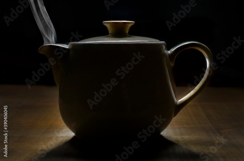 Tableau sur toile Steam coming out of a tea pot on a wooden table, in the dark, with black background and a back lit, rim light, chiaroscuro dark food photography style