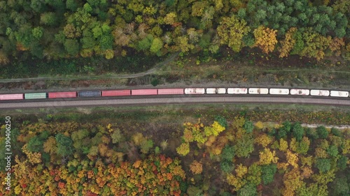 Top aerial view of a freight train moving through a beautiful autumn forest.