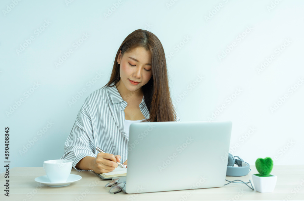 portrait a beautiful young woman taking notes and learning online with a laptop sitting in a table in the living room at the home office, work from home concept. portrait a beautiful young woman taking notes and learning online with a laptop sitting in a table in the living room at the home office, work from home concept.