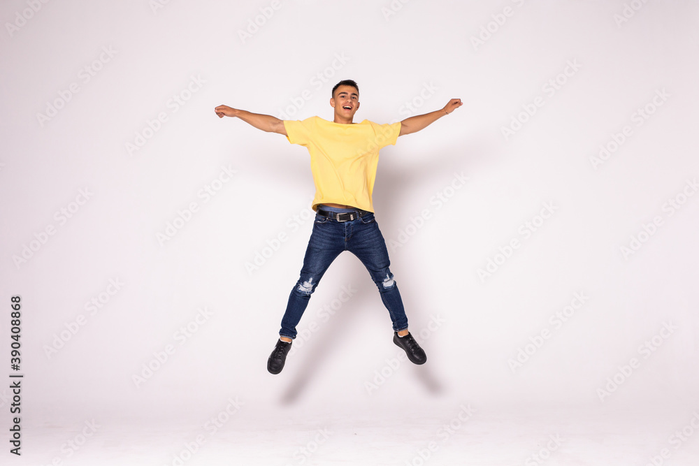 Young casual man celebrating his success and jumping over gray background.