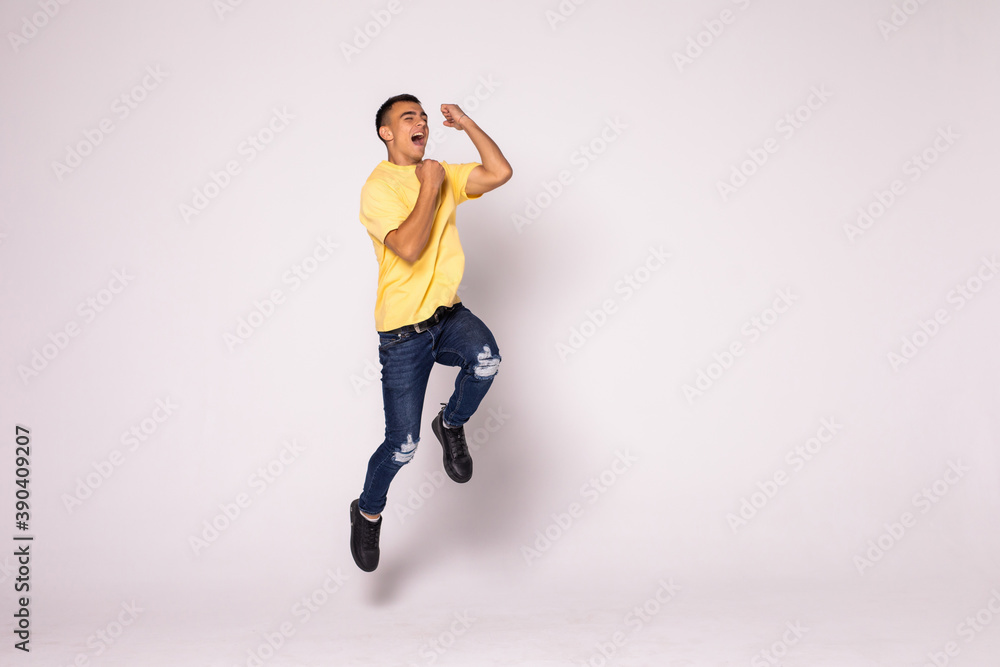 Young casual man celebrating his success and jumping over gray background.