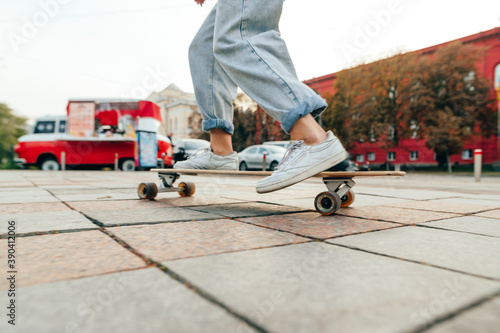 Close up blurred photo in motion, woman riding at speed on a longboard down the street against the backdrop of cityscape. Legs of a skater woman on a longboard walk.