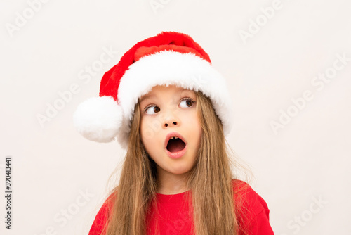 A beautiful little girl in a Christmas hat opened her mouth in surprise.