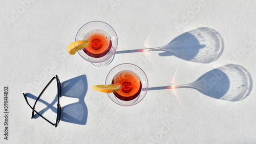 Top down shot of two cocktails close to a pair of glasses on an out of focus light background. Lifestyle and leisure concept.