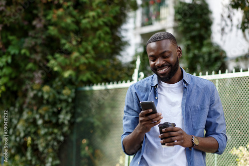 Happy man using mobile phone apps, texting message, browsing internet, looking at smartphone. Handsome Afro-American man using smartphone and smiling. Young people working with mobile devices.