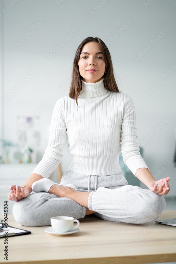 Young woman sitting on desk in padmasana yoga pose home office. Young woman sitting on desk in padmasana yoga pose home office.