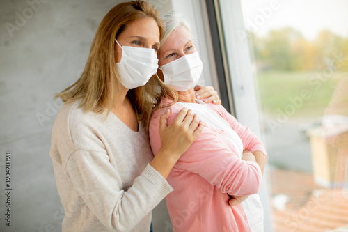 Senior woman with caring daughter at home wearing medical masks