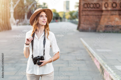Photography Female solo traveler holding a vintage camera while walking around the city of Barcelona in a nice outfit with a hat