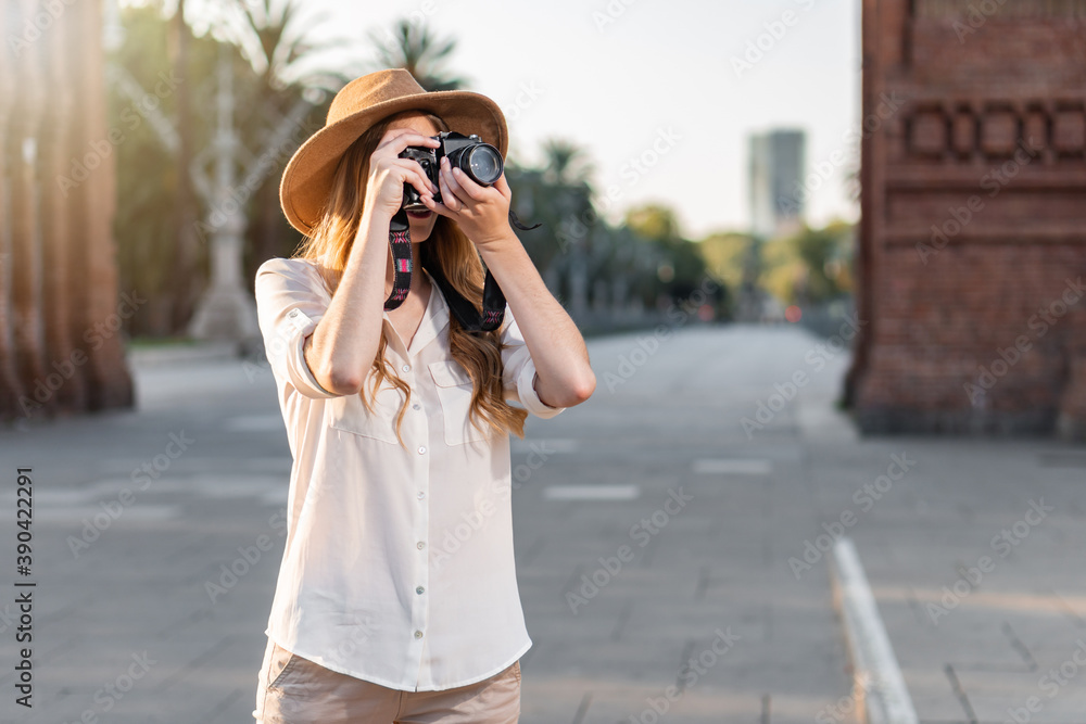 Beautiful woman in explorer outfit traveling and taking pictures with vintage camera. Freelance photographer working outdoors in Barcelona.