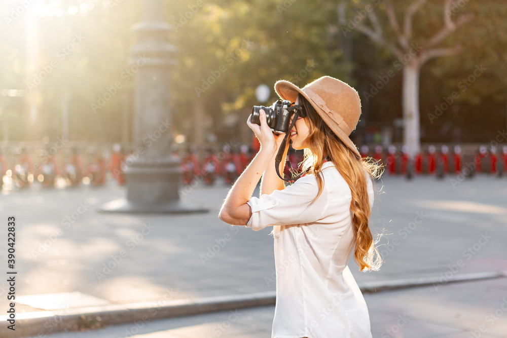 Beautiful woman in explorer outfit traveling and taking pictures with vintage camera. Freelance photographer working outdoors in Barcelona. Portrait at sunset in summer