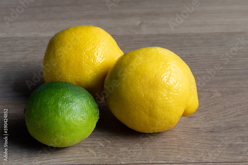 Two yellow lemons and a green lime on a wooden table