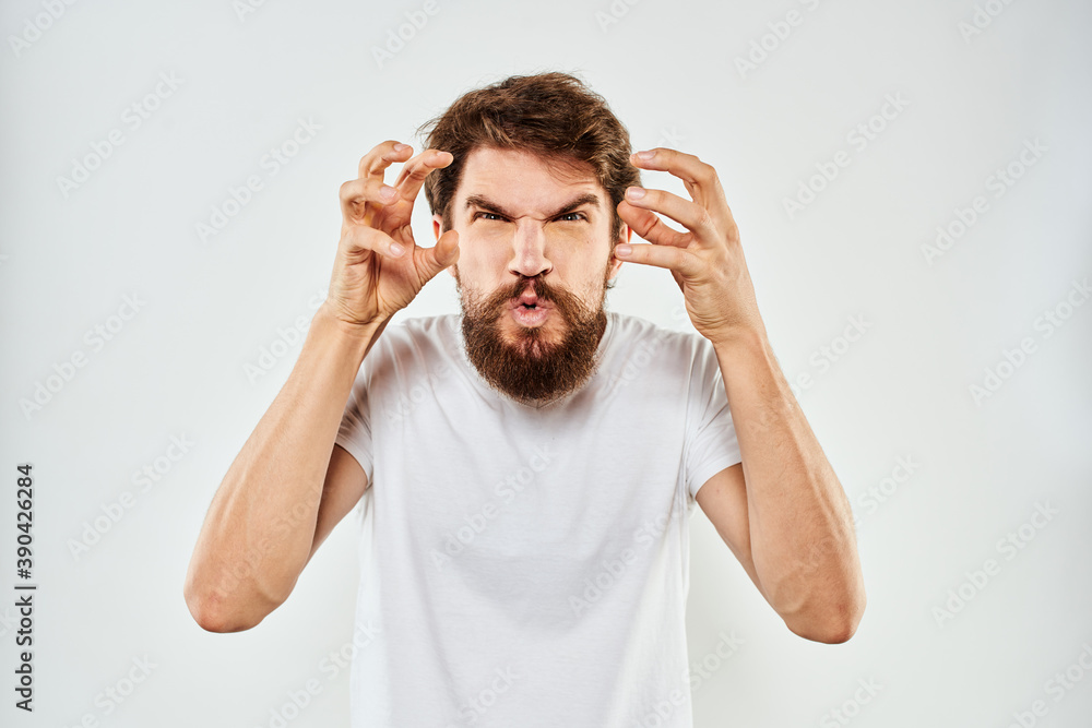 Naklejka premium Emotional bearded man in a white t-shirt gestures with his hands light background