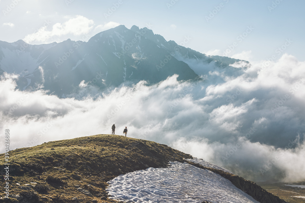 Unidentified tourists with large backpack stands on high mountain cliff at level of clouds