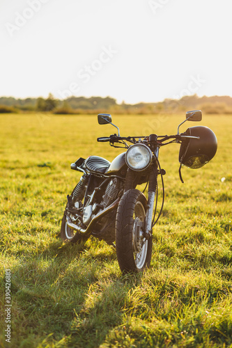 classic black motorcycle and helmet in a field at sunset
