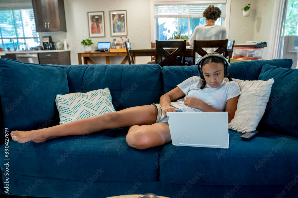 Obraz premium Girl in wireless headphones home schooling with laptop computer on couch. 