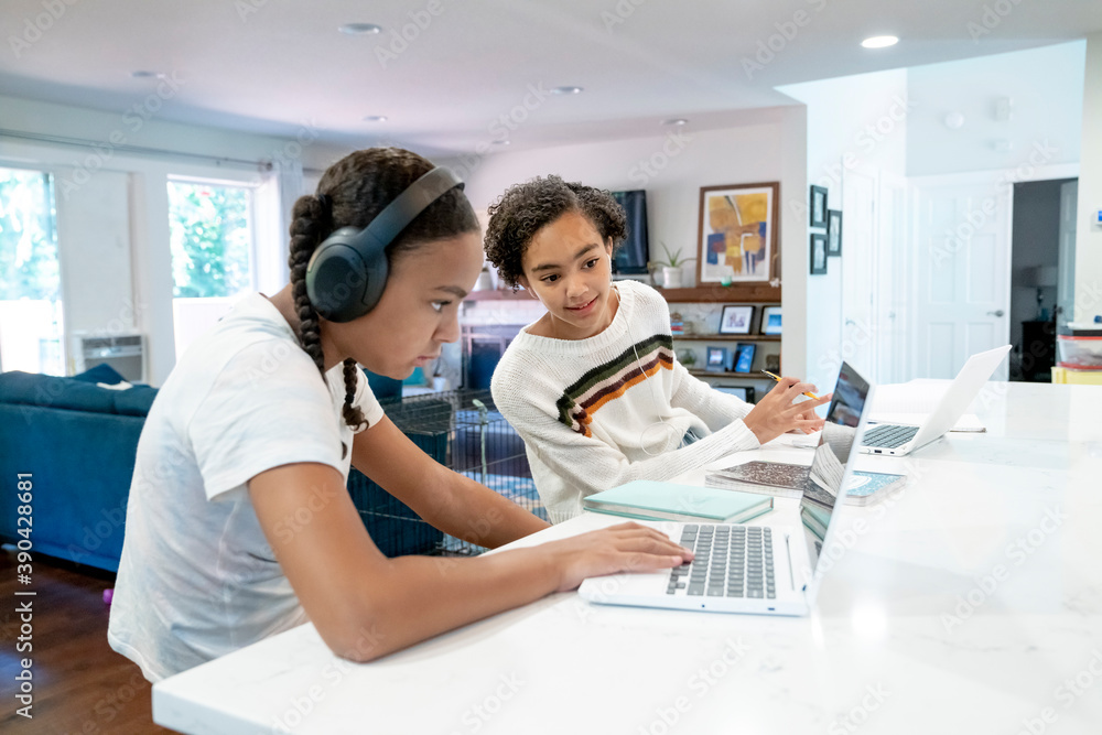 Fototapeta premium Sisters home schooling on laptop computers in kitchen