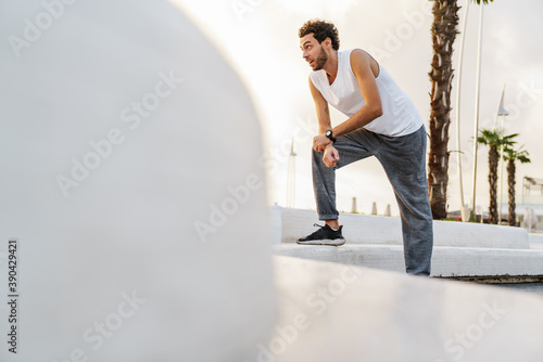 Focused unshaven sportsman resting while working out on promenade
