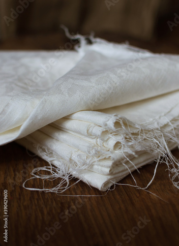 Stack of old white linen fabric on dark wooden table, selective shallow focus, vintage style