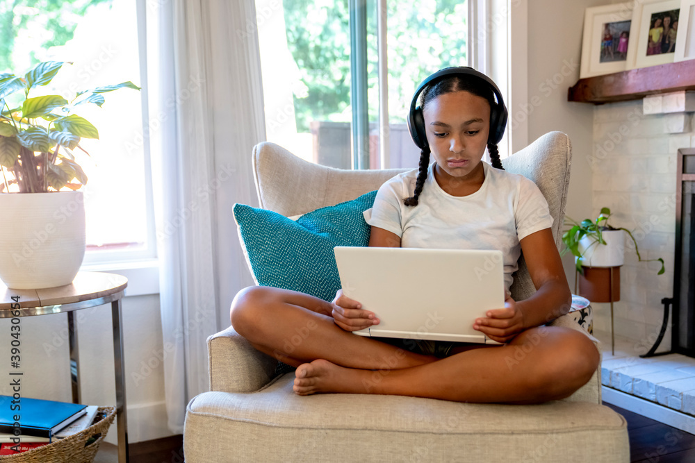 Girl in wireless headphones sitting in living room doing home school work on laptop Girl in wireless headphones sitting in living room doing home school work on laptop