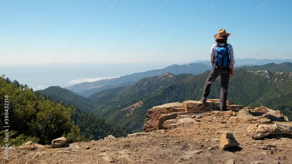 Woman hiker overlooking the ocean in Big Sur, California waves her hat in triumph Woman hiker overlooking the ocean in Big Sur, California waves her hat in triumph
