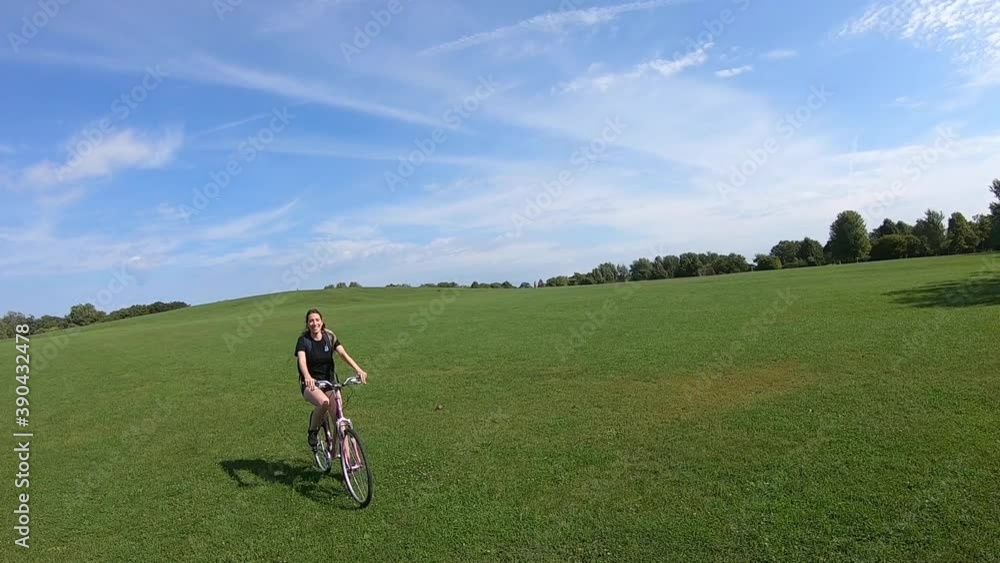 Happy young woman riding a bike in a park on a sunny day with a blue sky and beautiful clouds. Funny moment. Slow motion. Happy young woman riding a bike in a park on a sunny day with a blue sky and beautiful clouds. Funny moment. Slow motion.