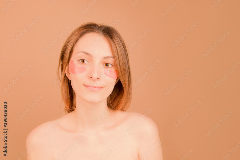 Obraz premium The concept of cosmetic skin care under the eyes. Girl with patches under the eyes on a brown background.